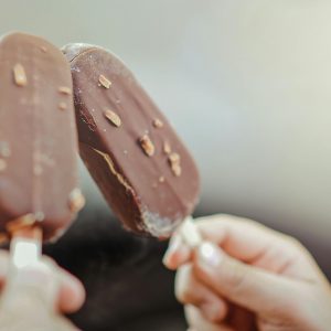 Close-up of two chocolate ice cream bars with nuts held by hands.